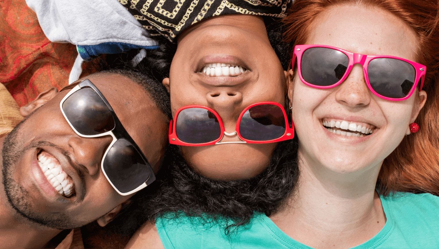 Multicultural friends wearing pink and orange sunglasses lying down