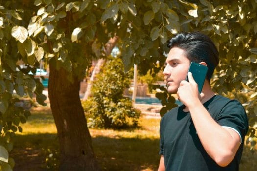 Man in black shirt walking in park using phone for urgent cash loans